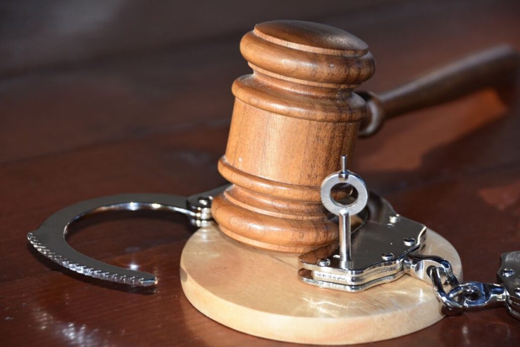 木製の裁判官用ガベルと手錠、鍵が机の上に置かれた司法・逮捕を象徴するイメージ