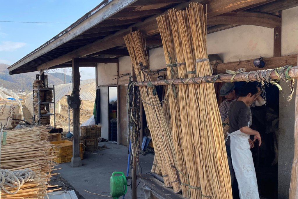 木造の作業場で束ねた植物繊維を干しながら職人が作業している様子
