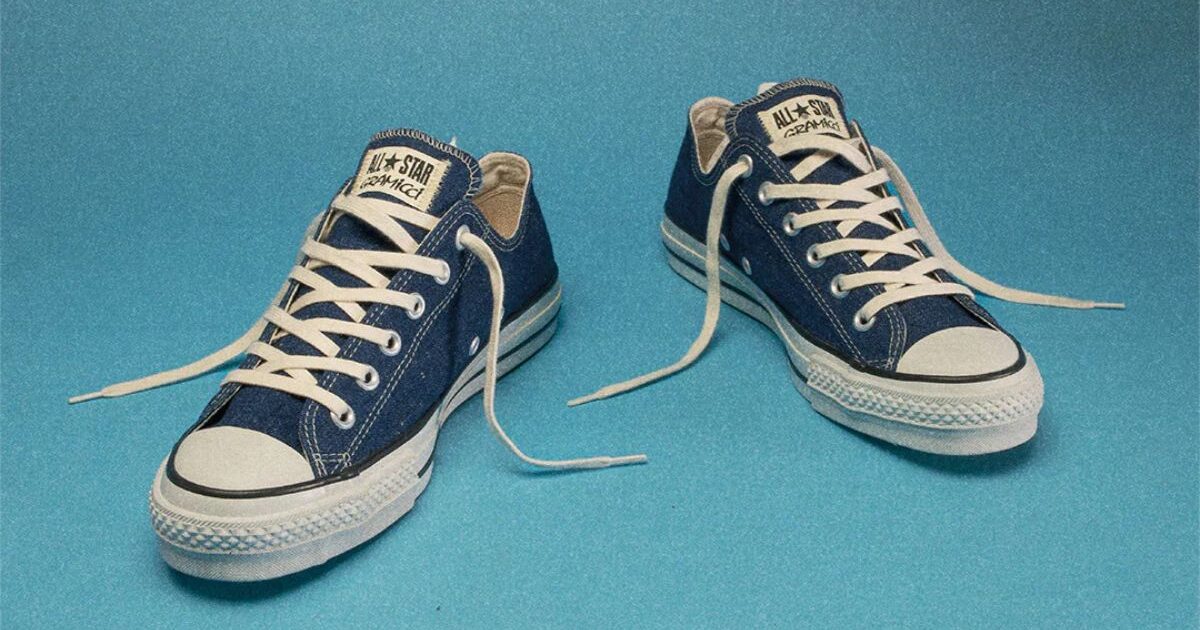 青いデニム生地のコンバース オールスター（Converse All Star）スニーカー。白いレースと白いラバーソールが特徴のクラシックな一足が、明るい青色の背景に並べて置かれている