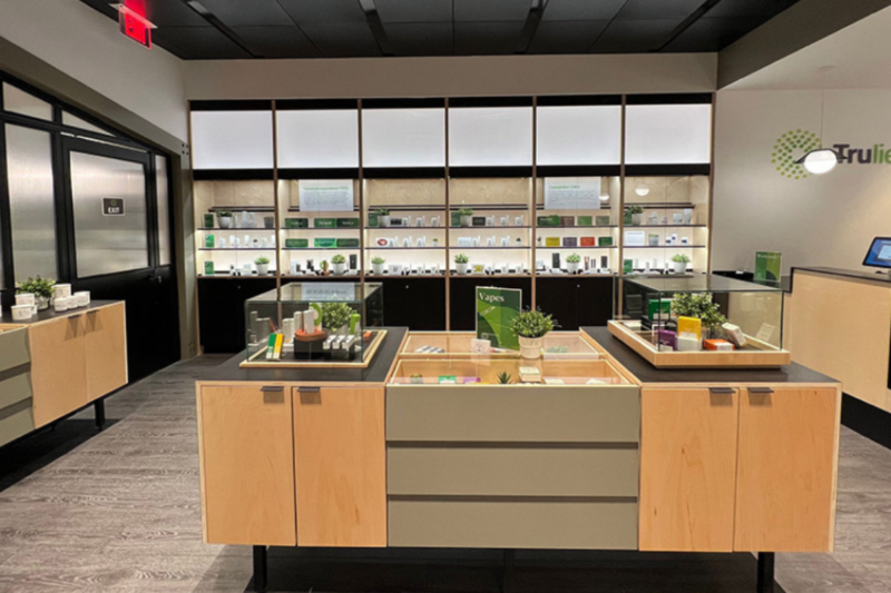 Trulieve（トゥルーリーヴ）の大麻ディスペンサリー（大麻薬局）の店内。明るい木製の什器、ガラス張りのディスプレイケース、そして背面には棚に並べられた製品が美しく陳列されている。店内は現代的で清潔感がある。