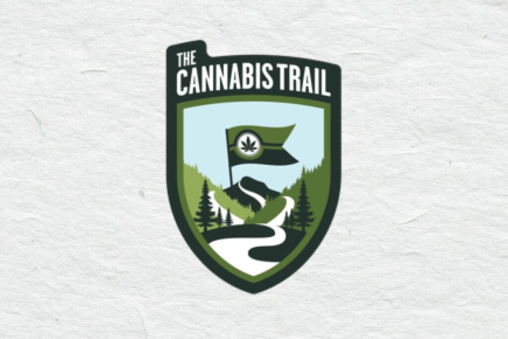 白い和紙のような質感の背景に配置された盾型ロゴ「THE CANNABIS TRAIL」。上部に白い文字、中央に水色の空、緑の山と松の木、白い曲がりくねった道、山頂に大麻の葉が描かれた旗が立つイラスト。